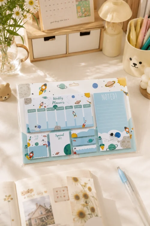 Space Weekly Planner Sticky Notes Set with rockets, planets, weekly planner, memo pads, sticky notes, page markers, and to-do list on a wooden desk.